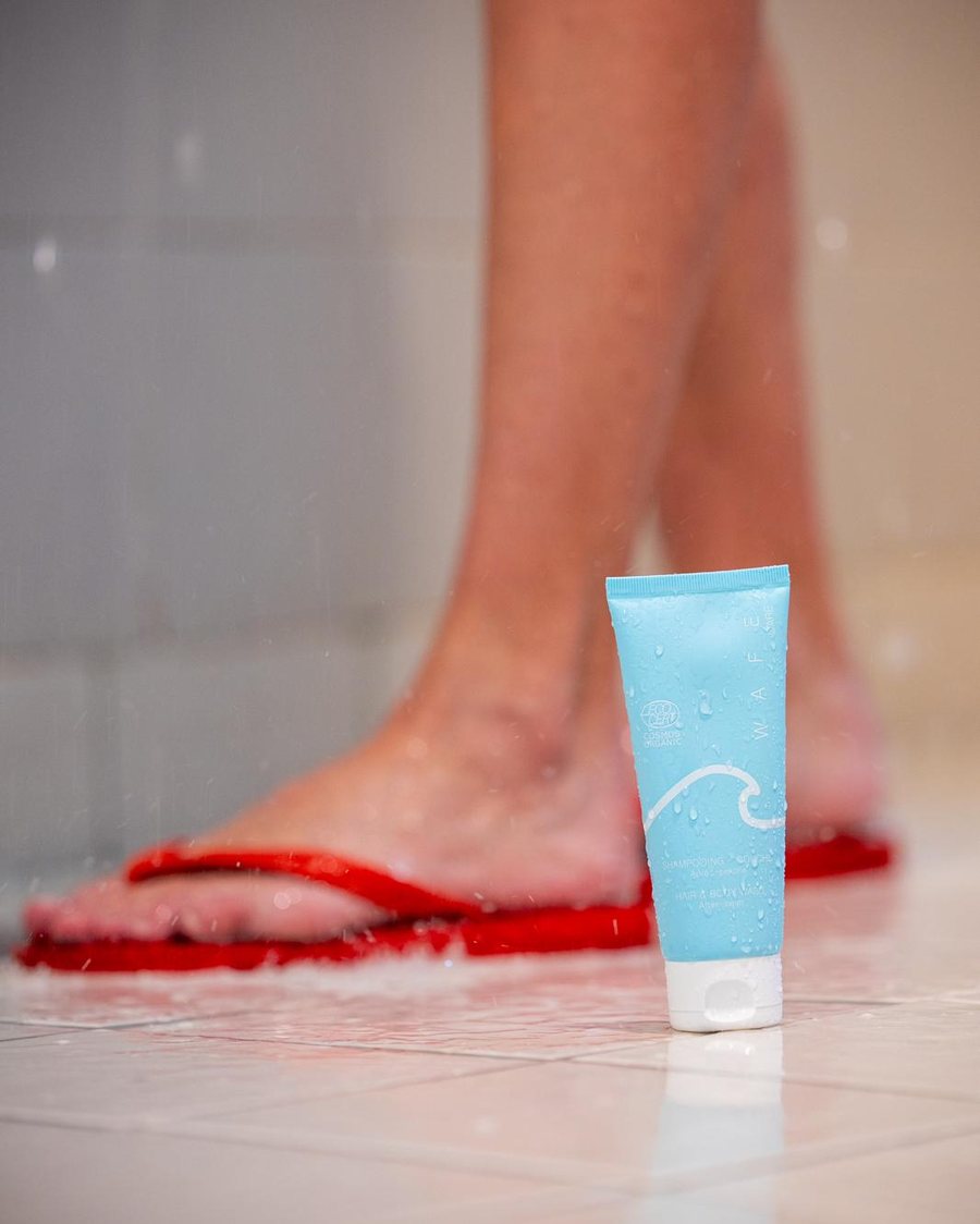 Le shampooing-douche WAFE Care posé sur le carrelage de la douche, à côté de pieds en tongs